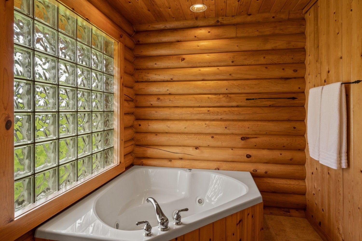 Cozy wood-paneled bathroom with a corner jetted tub and a glass block window