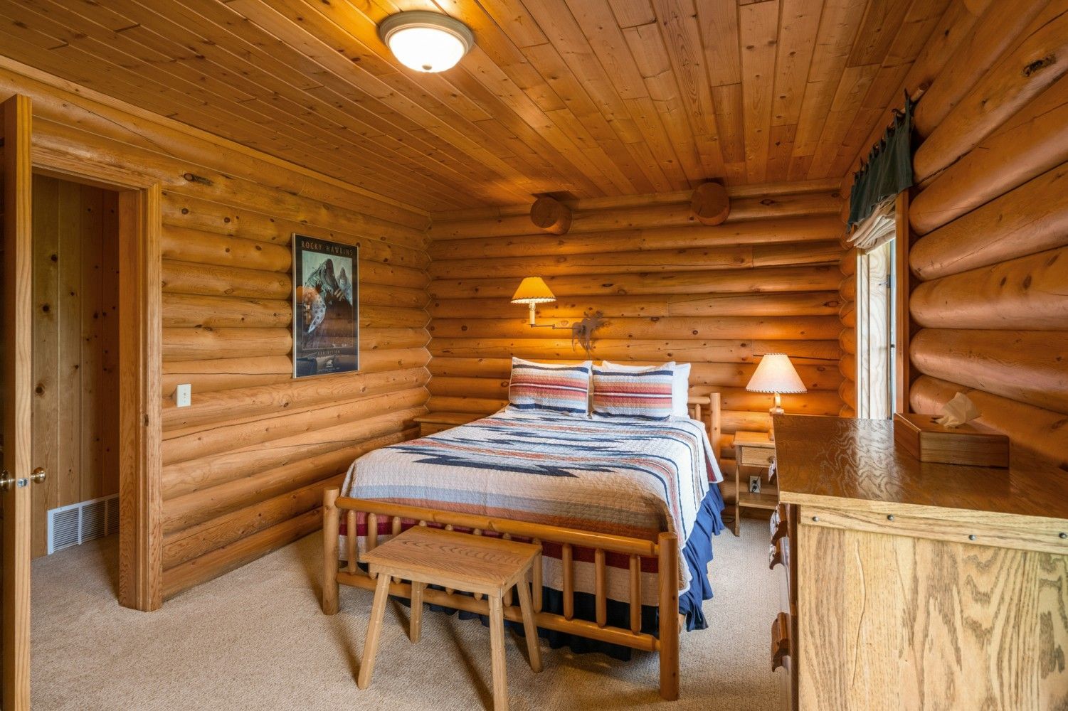 Cozy log cabin bedroom with a bed, bedside lamps, and wood-paneled walls and ceiling