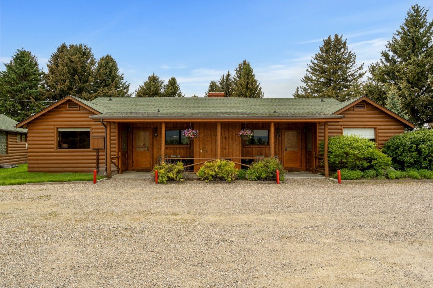 Rustic log cabin storefront with green roof and gravel parking under a clear blue sky