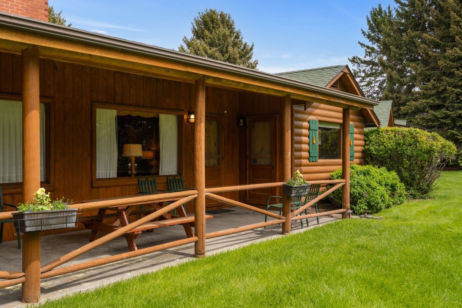 Wooden cabin with a covered porch and green lawn in bright sunlight