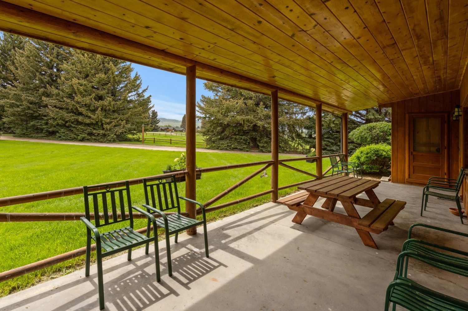 Covered porch with green chairs, picnic table, and a view of a grassy yard and trees