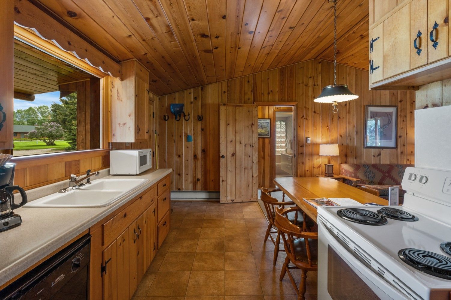 Wood-paneled cabin kitchen with white stove, wooden cabinets, and a dining table by the window