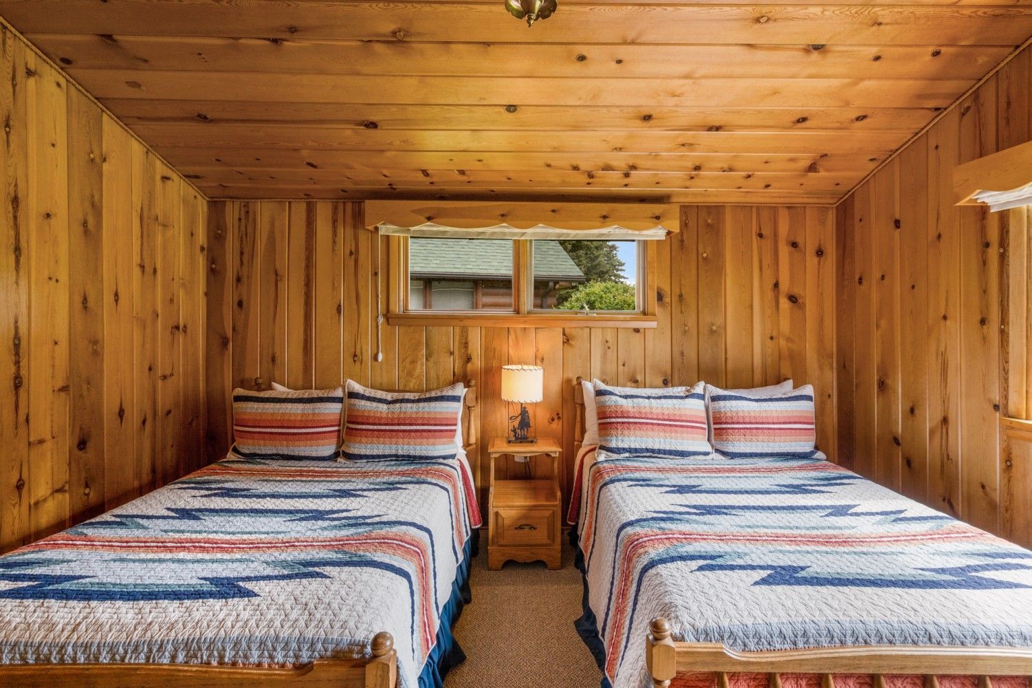 Wood-paneled cabin bedroom with two twin beds, striped quilts, and a small window between them