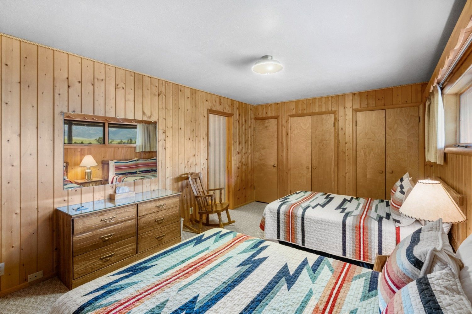 Wood-paneled bedroom with striped rug, bed, dresser, and chair by a window