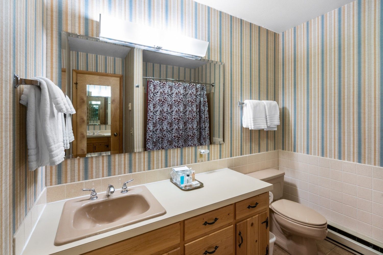 Bathroom vanity with striped wallpaper, mirror, sink, towel rack, shower curtain, and toilet.