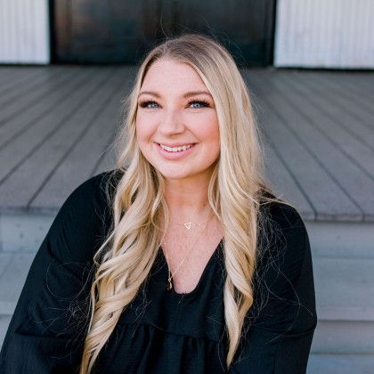 A woman is sitting on a set of stairs wearing a black shirt and smiling.