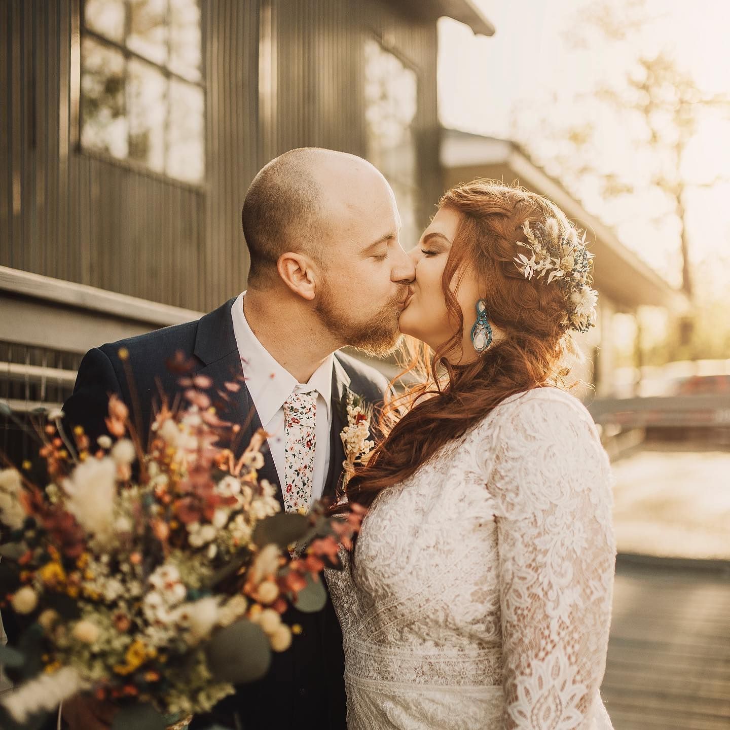 A bride and groom kissing on a bridge while holding a bouquet of flowers.