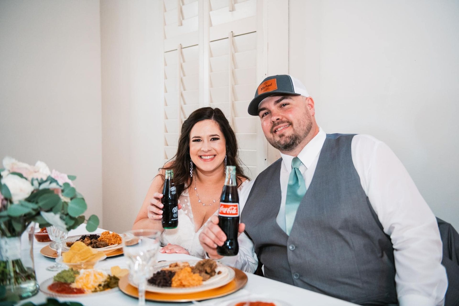 A bride and groom are sitting at a table holding coca cola bottles.