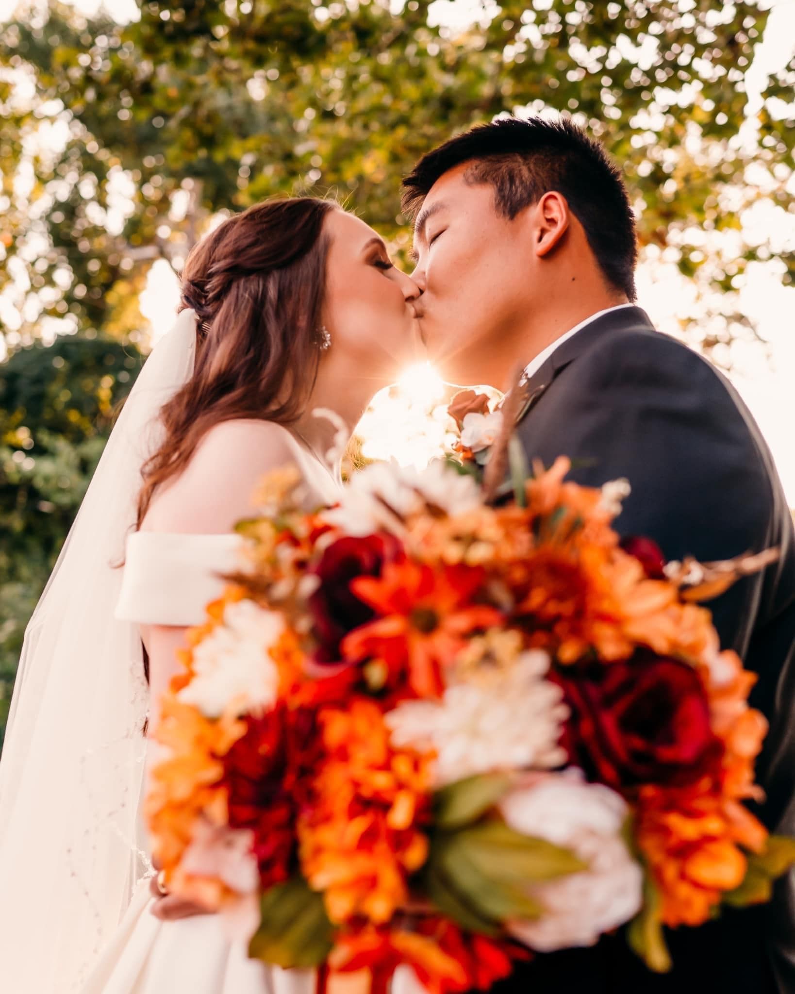 A bride and groom kissing in front of a bouquet of flowers.