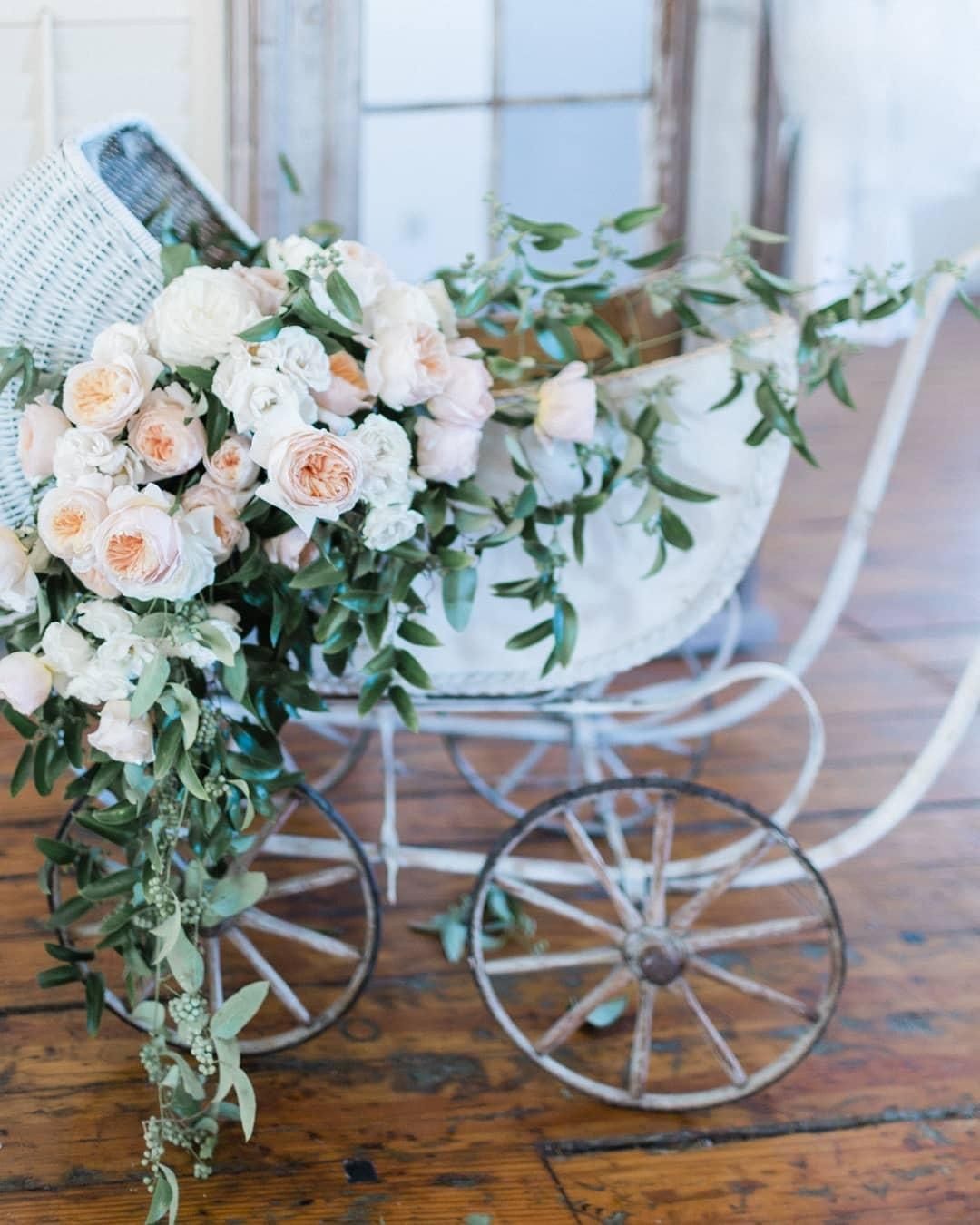 A white baby carriage filled with flowers is sitting on a wooden floor.