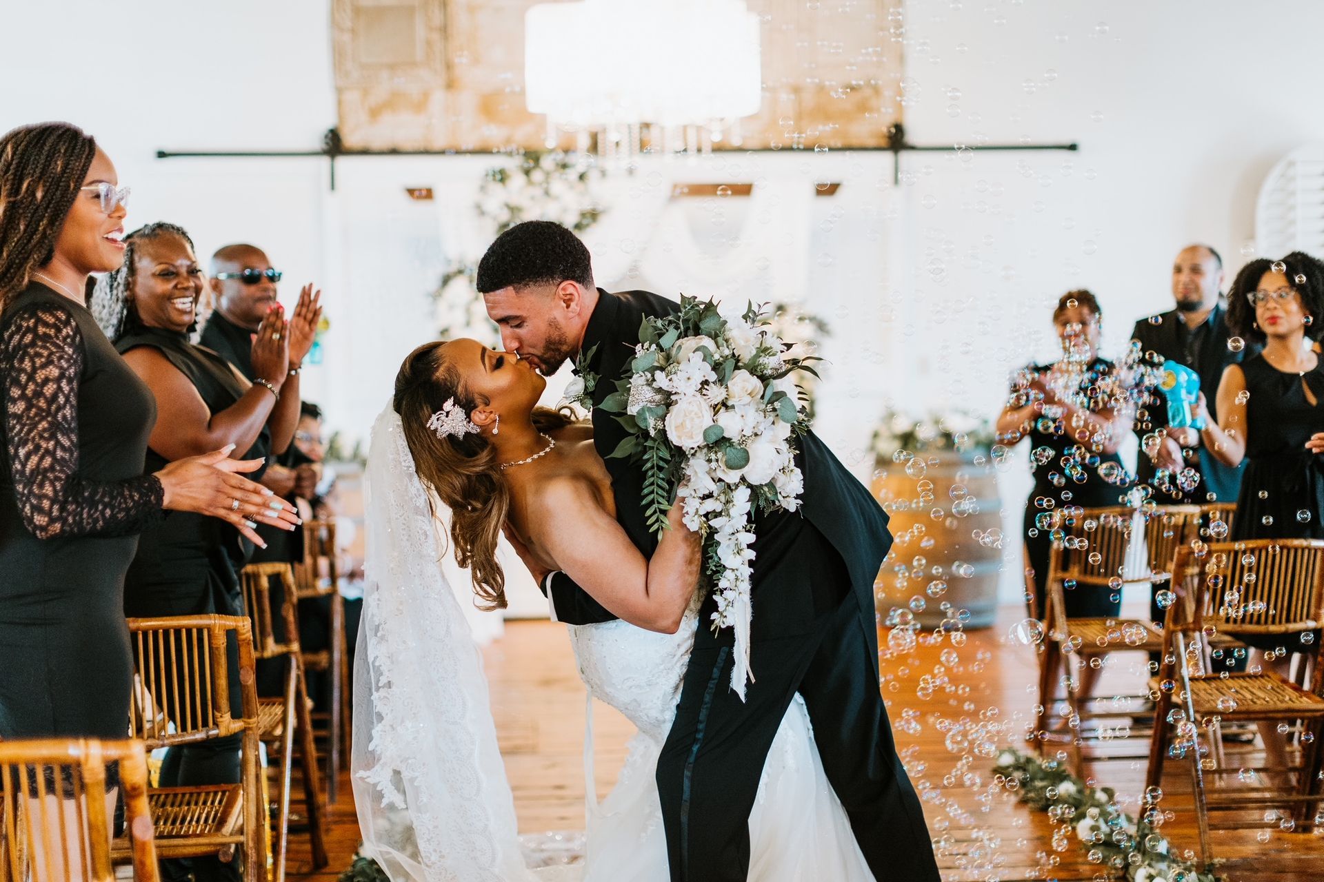 A bride and groom are kissing in front of their wedding guests.