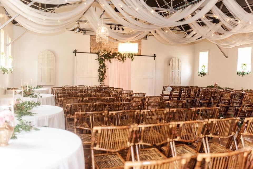A large room with rows of wooden chairs and tables set up for a wedding ceremony.