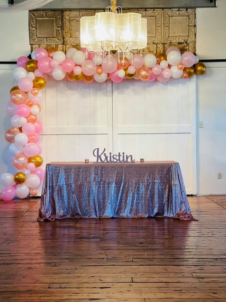 A table with a sequined tablecloth and balloons behind it.
