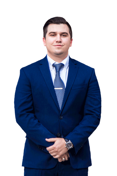 A man in a blue suit and tie is standing with his hands folded.