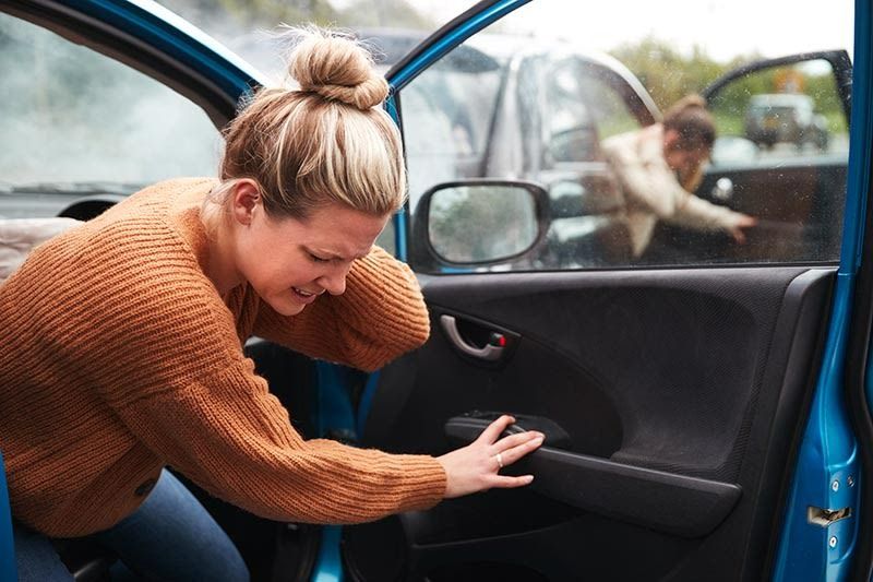 A woman is sitting in a car after a car accident.