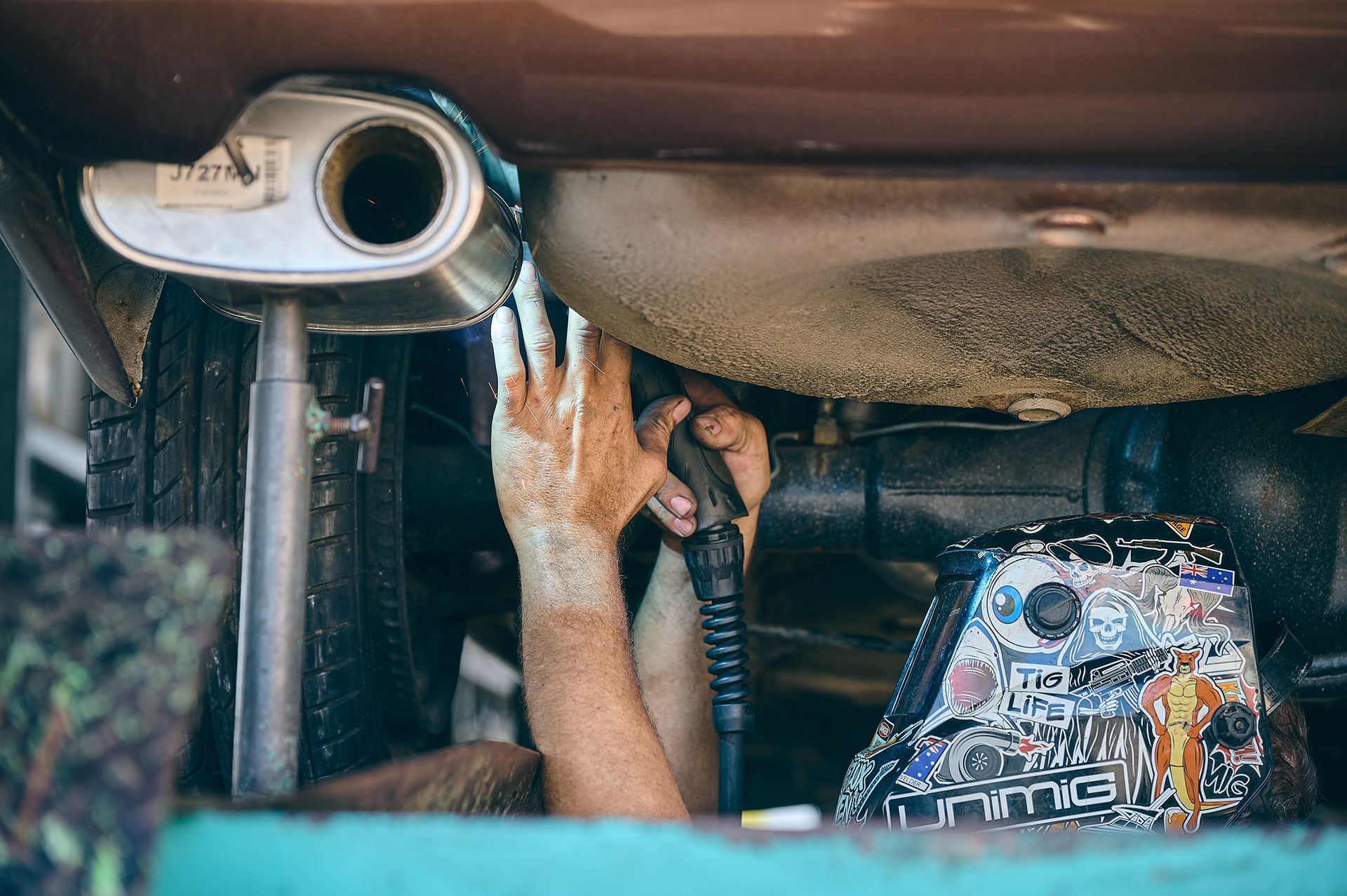 Person Working on Car's Exhaust — Gladstone Mufflers & Suspension In Gladstone Central, QLD