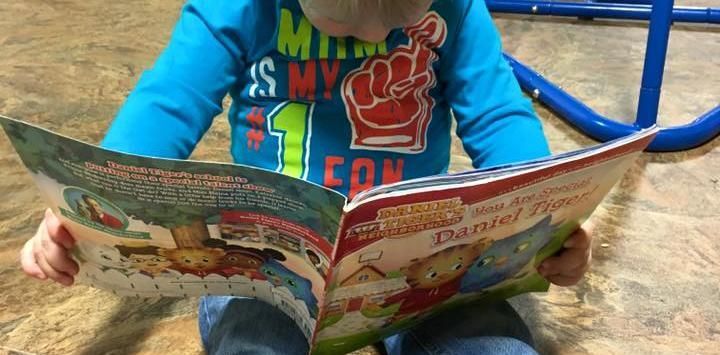 A person in a blue shirt holds and reads a Daniel Tiger children's book.