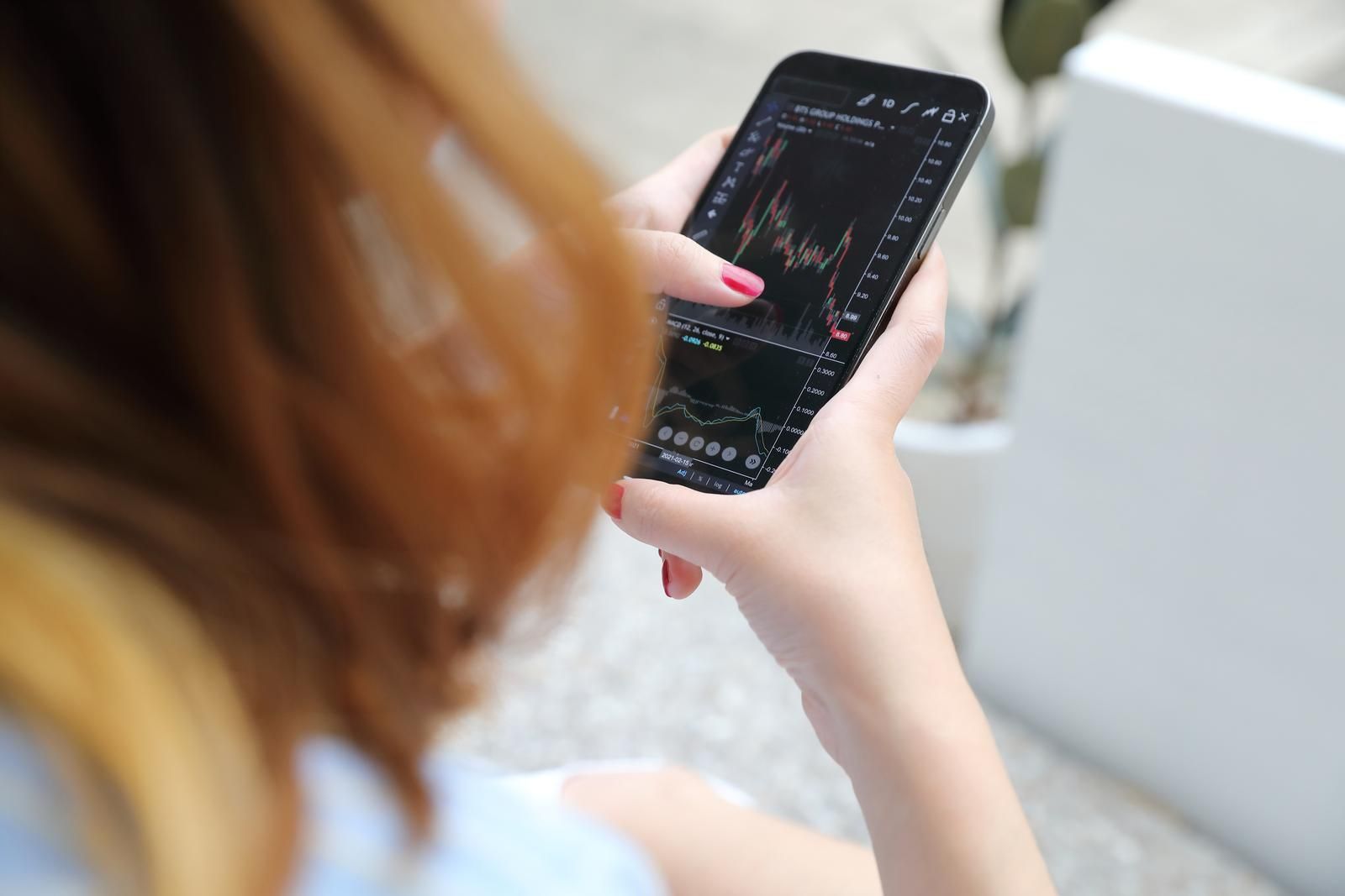Frau nicht vollständig sichtbar hält ein Smartphone mit Börsen Chartdaten