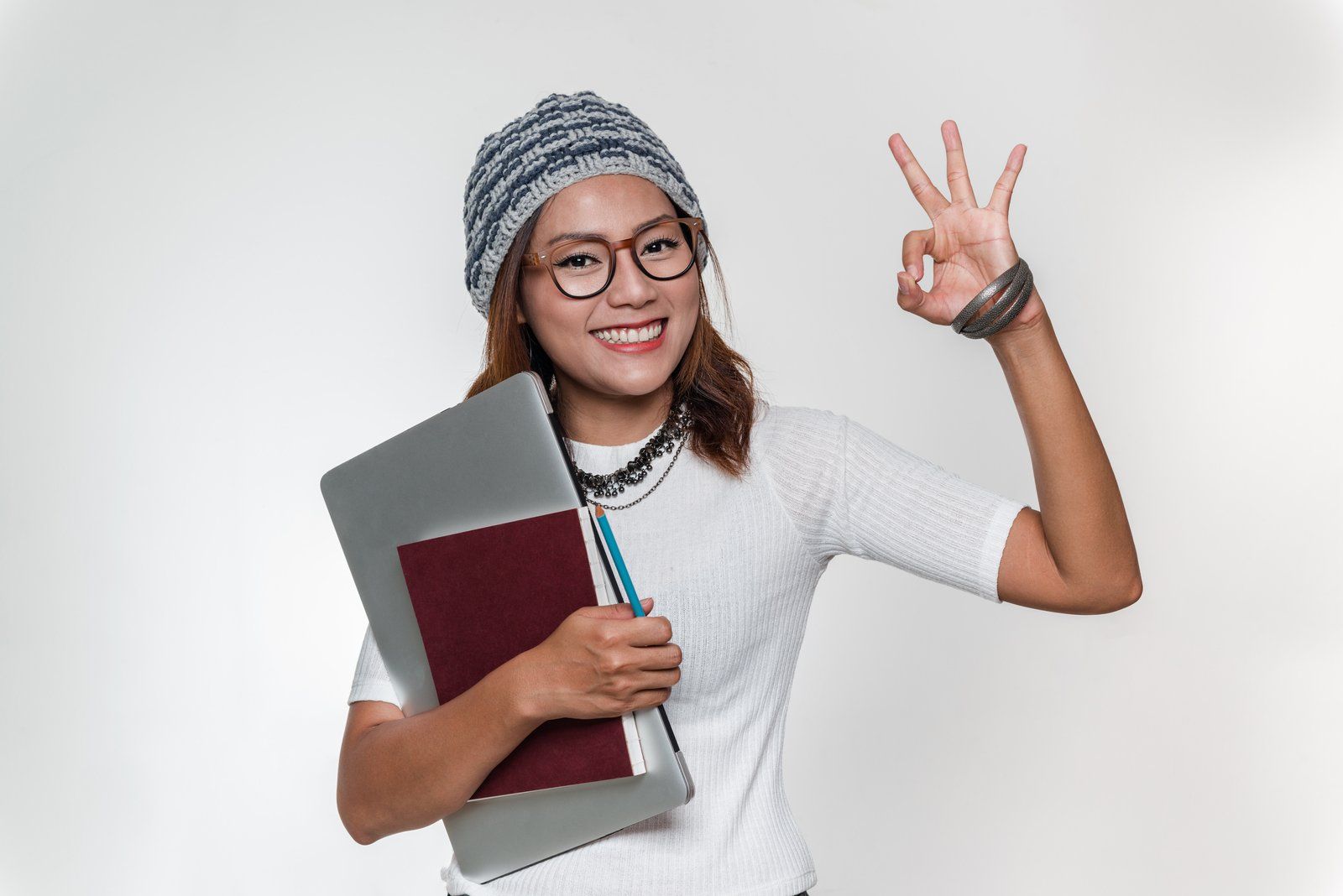 Eine Frau hält einen Laptop und Bücher und gibt ein OK-Zeichen.
