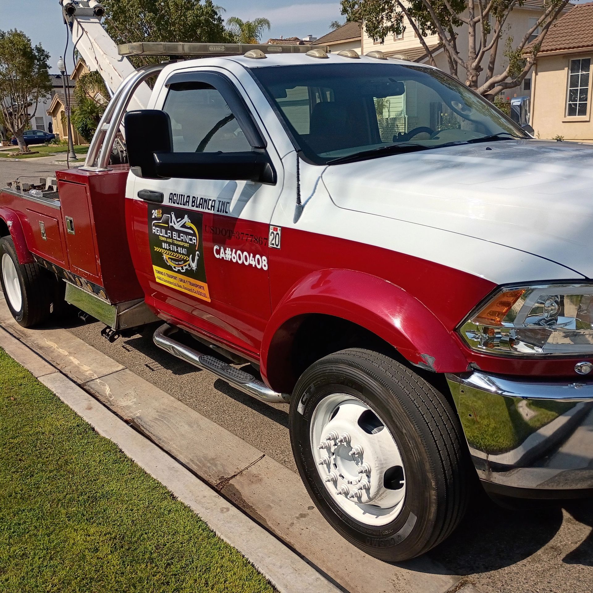 Red and white tow truck parked by a curb in bright sunlight