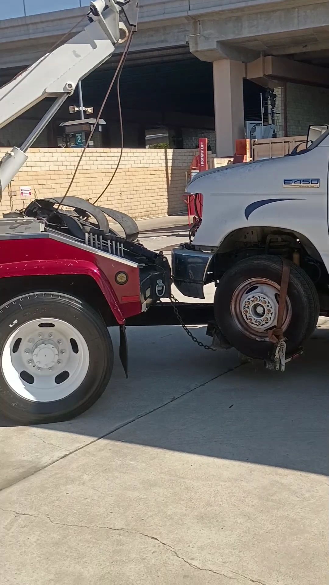 Tow truck loading a white pickup from a driveway under an overpass