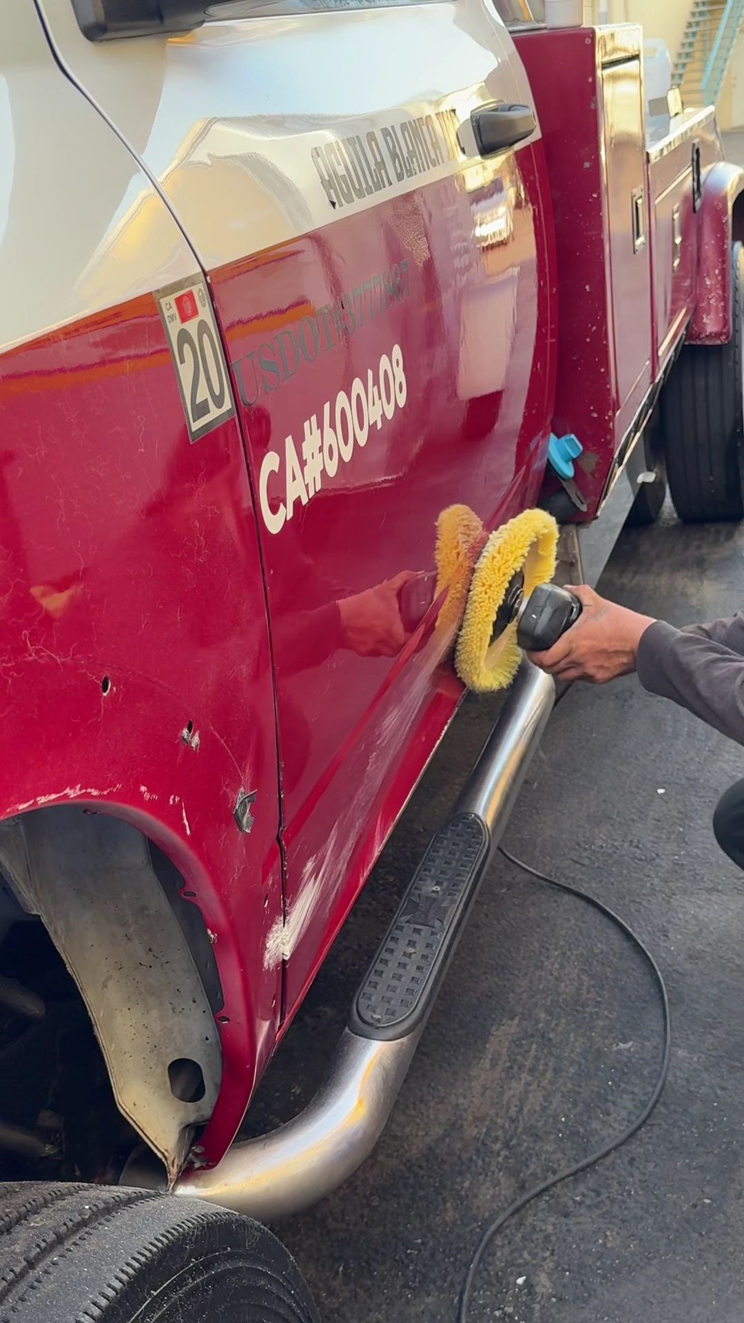 Person polishing the side of a red and silver truck with a yellow buffer pad