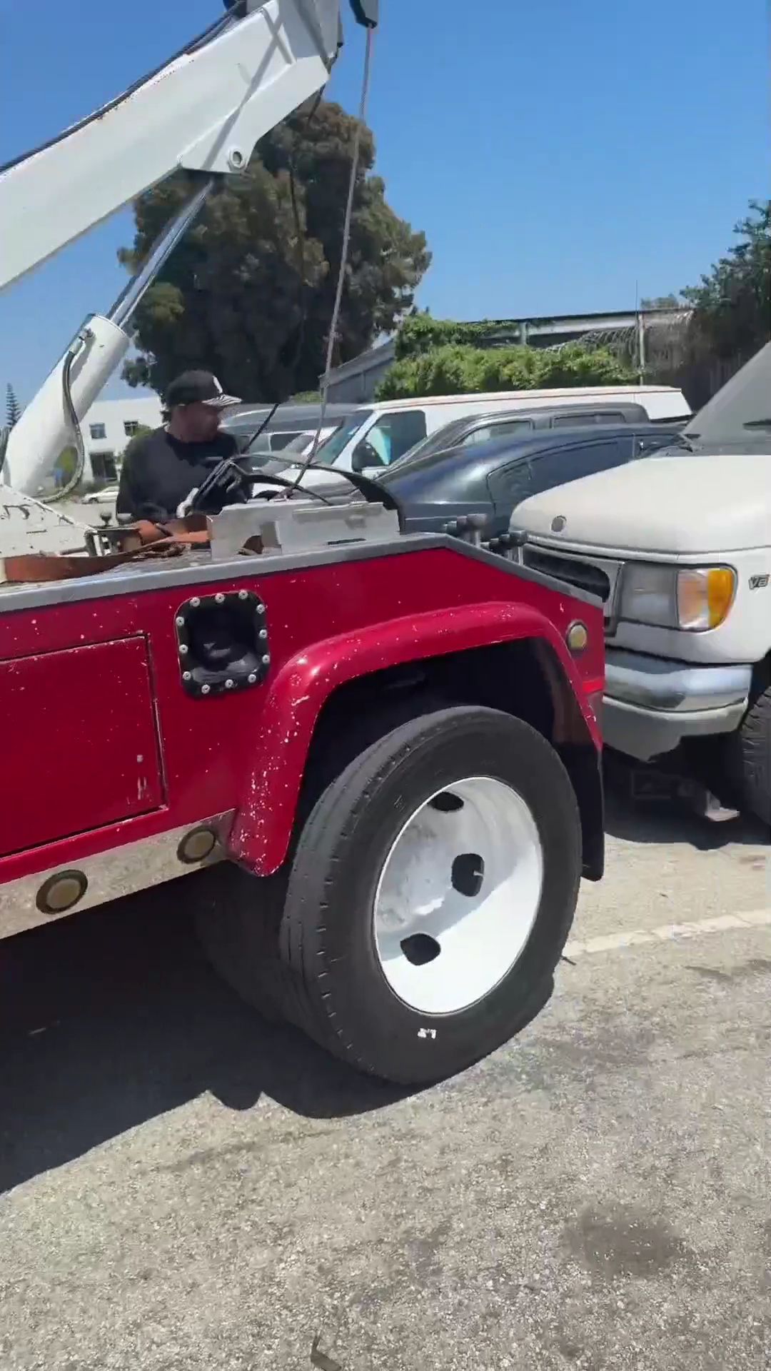 Red tow truck with a driver towing a silver SUV on a sunny street.