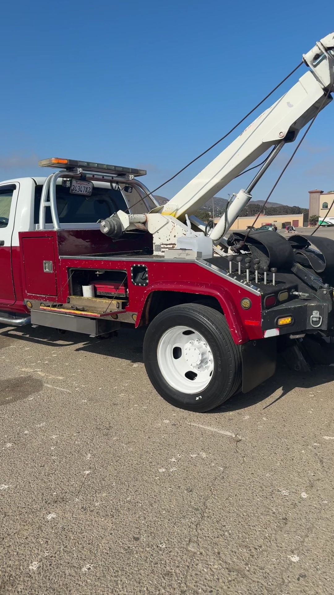 Red tow truck with raised boom parked on gravel lot under a clear blue sky.