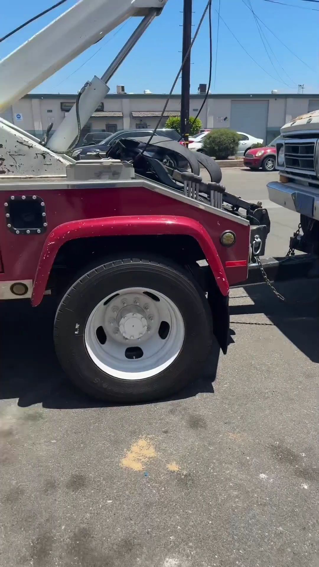Red tow truck with open hood parked in a lot beside another vehicle under a blue sky.