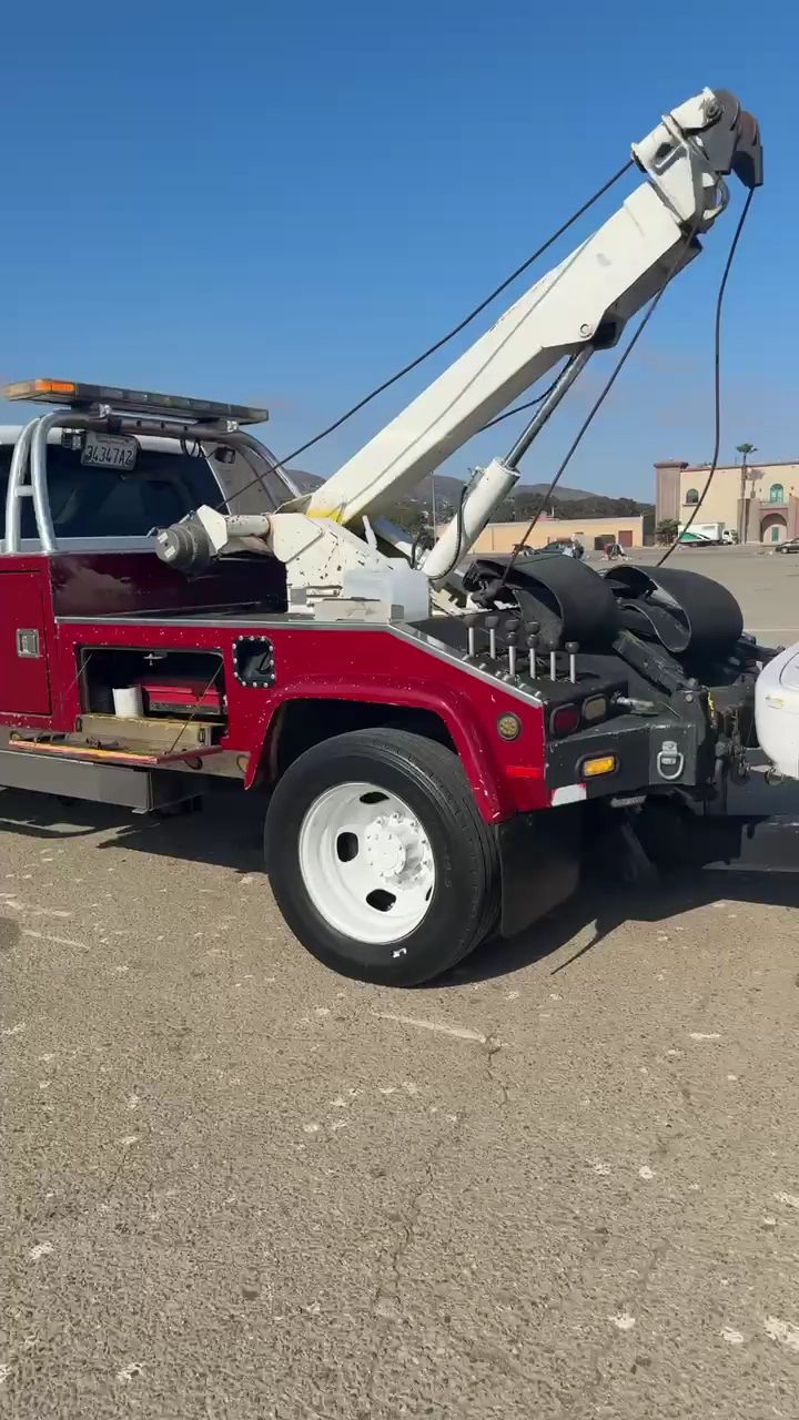 Red tow truck with white boom parked on gravel lot under a clear blue sky.