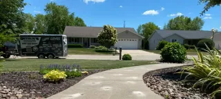 Curved front walkway leading to a suburban house with a parked van and landscaped yard under a clear blue sky