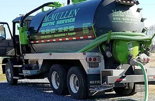 A McMullen Septic Service truck with a green and black tank pumping liquid. The truck is parked outside.