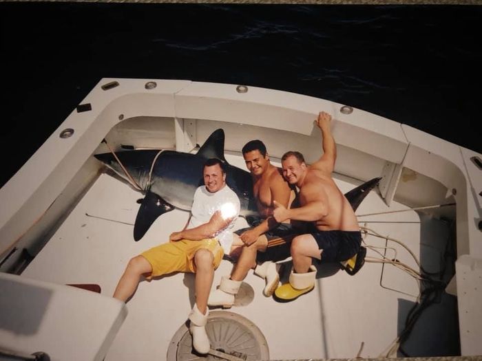 three men lying on a dead shark