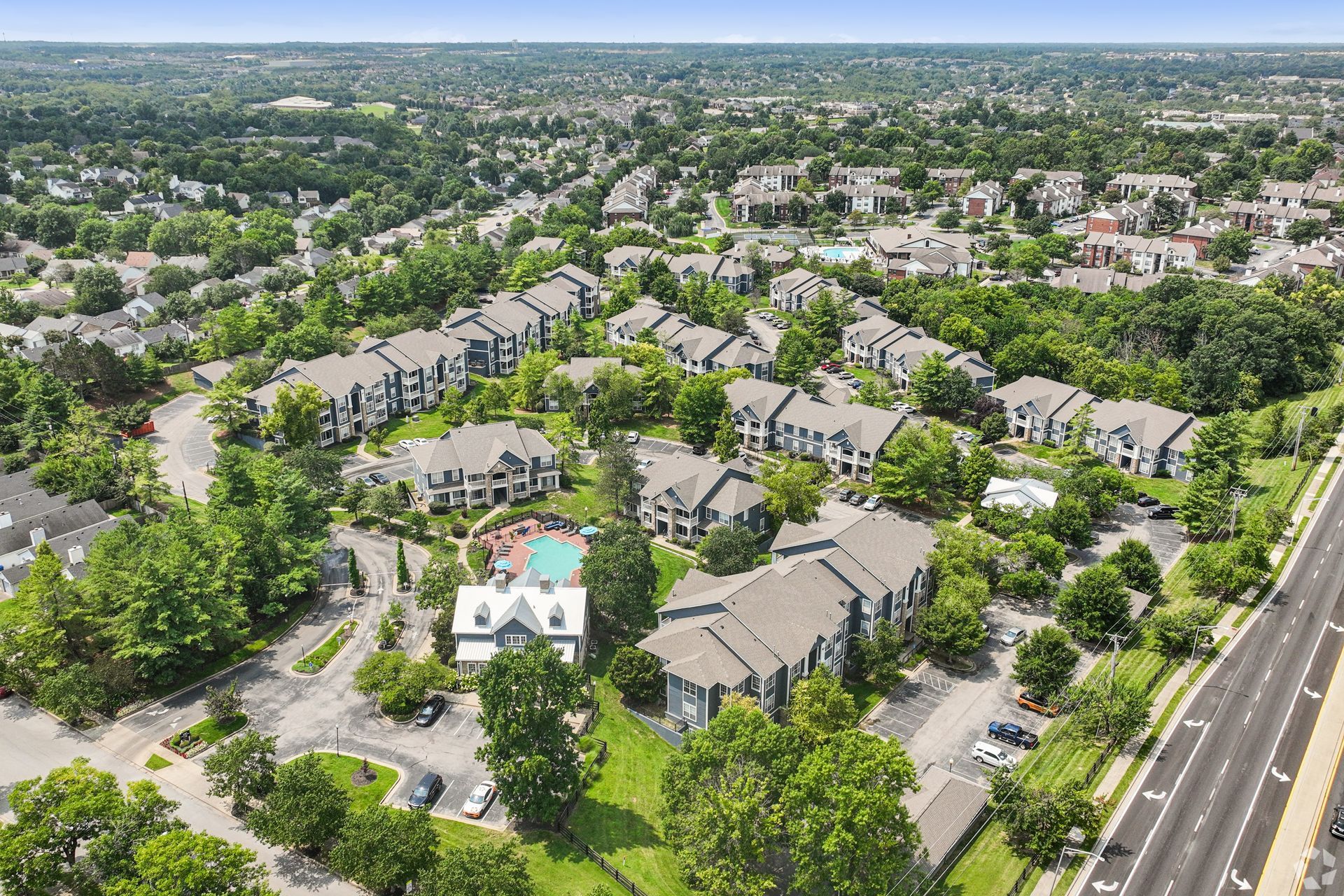 Aerial view of a suburban apartment complex with trees and parking lots.