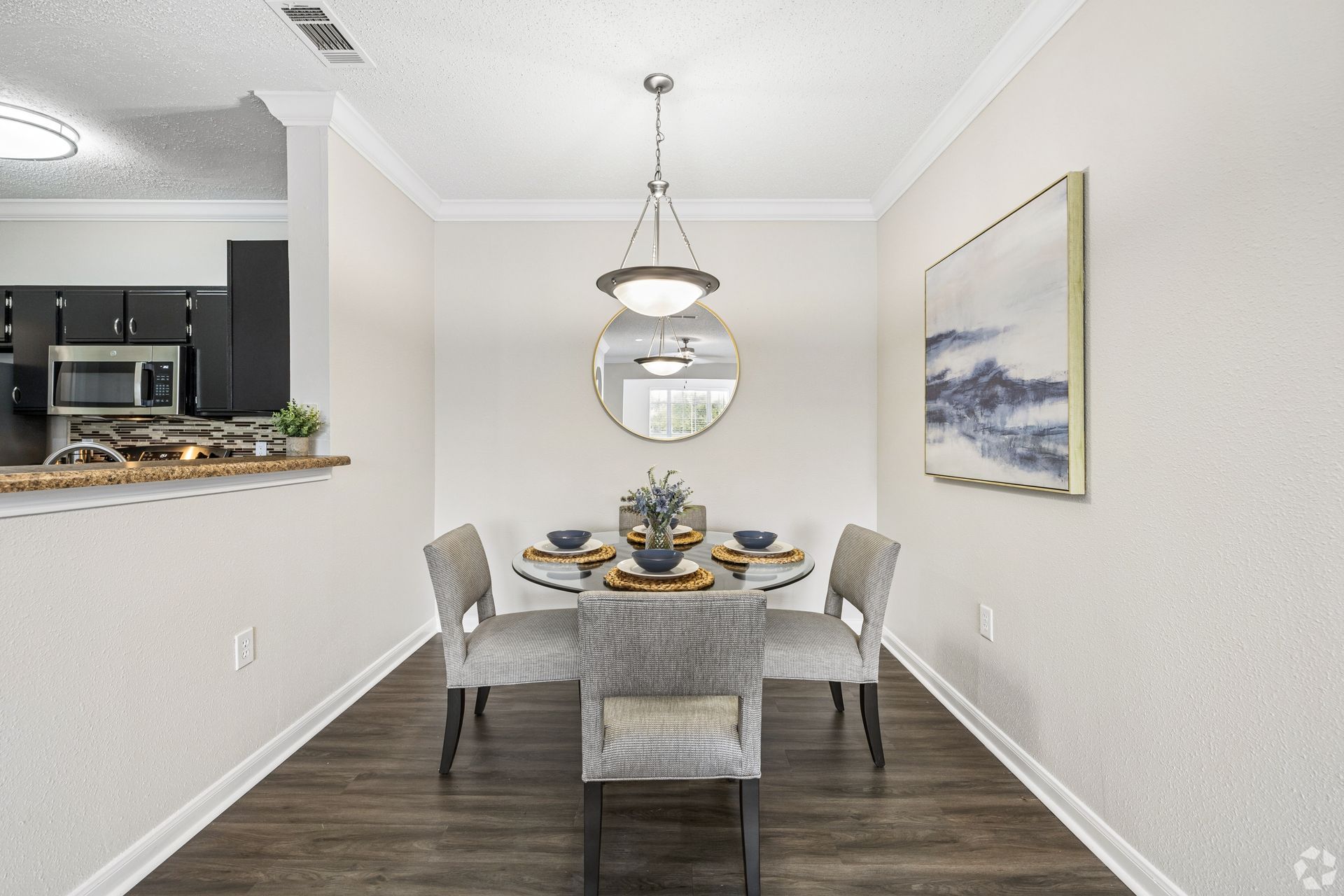 Modern dining room with a table set for four, gray chairs, dark wood-style floors, mirror, and a pendant light