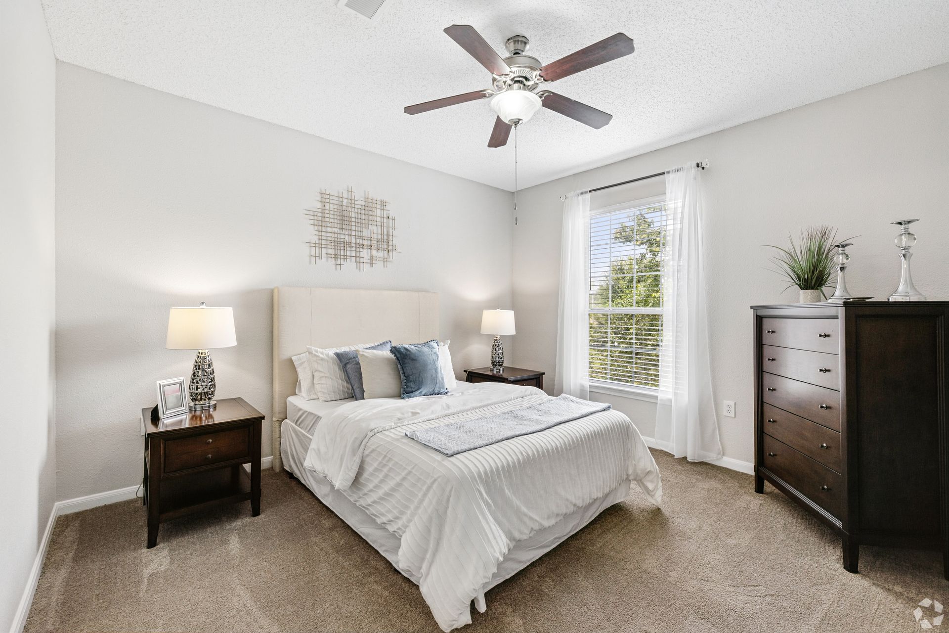 Bright bedroom with a bed, nightstands, dresser, ceiling fan, and a window.
