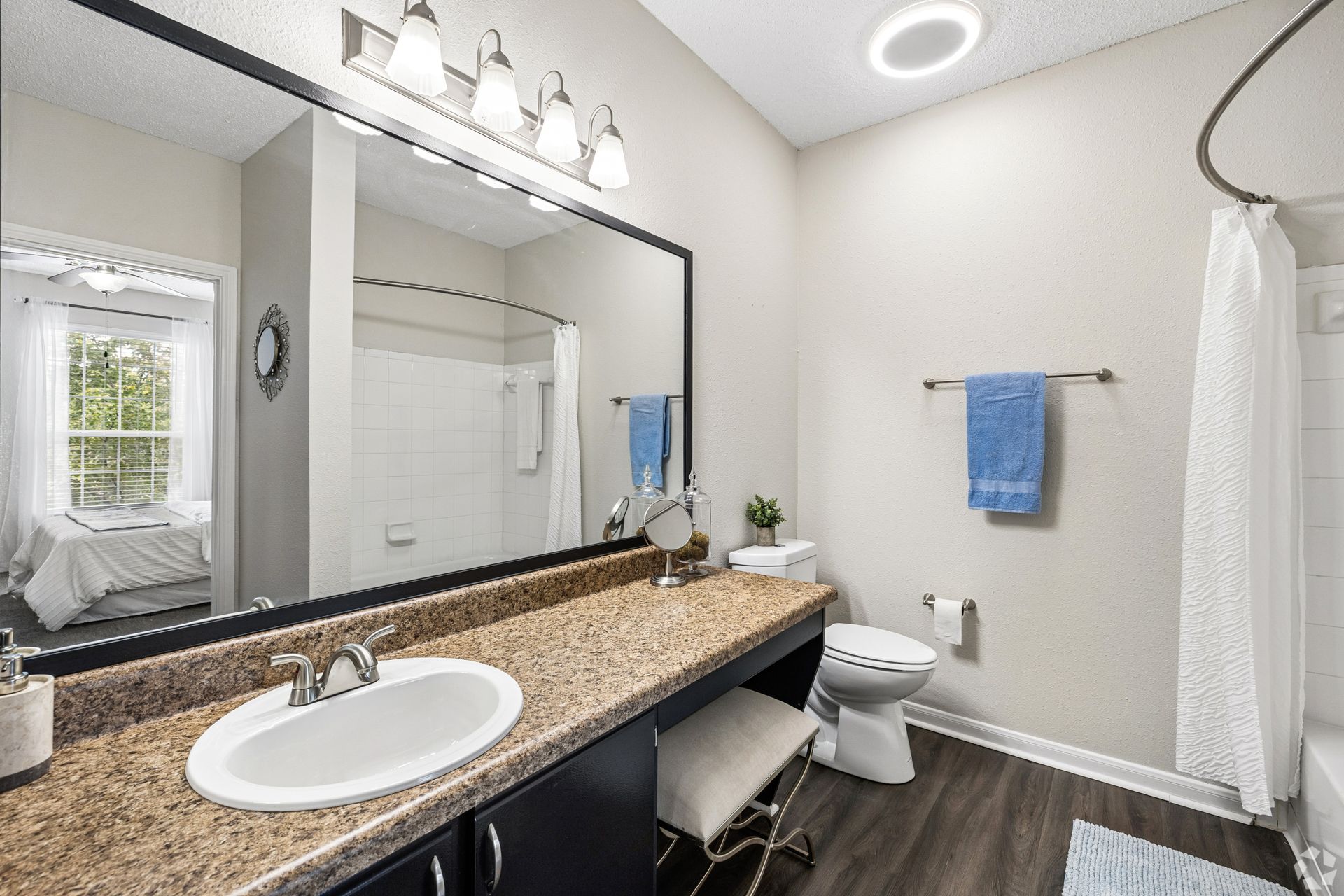 Modern bathroom with white walls, dark vanity, large mirror, sink, toilet, shower curtain, and blue towels.