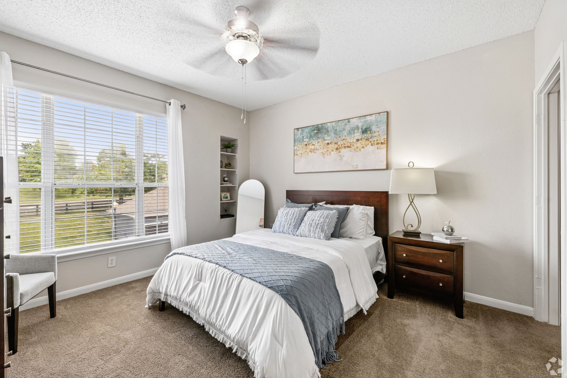 Bright bedroom with a bed, nightstand, large window, lamp, and ceiling fan.
