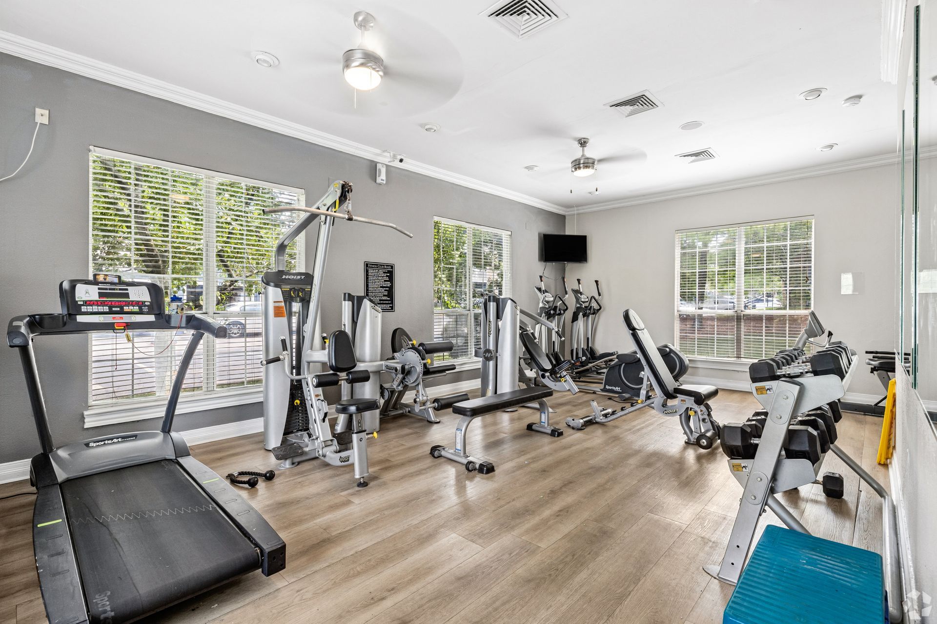 Bright home gym with treadmill, weight benches, exercise bike, and large windows