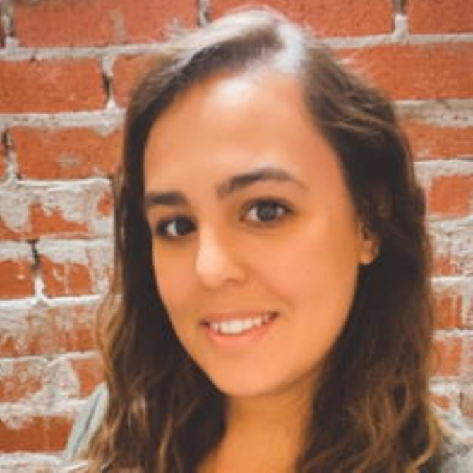 A woman is smiling in front of a brick wall.