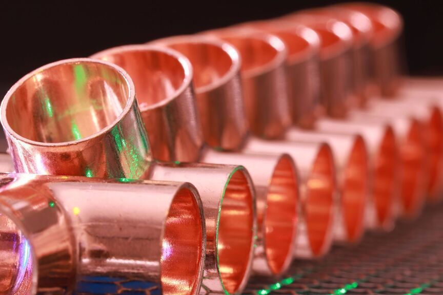 Copper-colored metal pipes aligned in rows, with one pipe tilted in the foreground