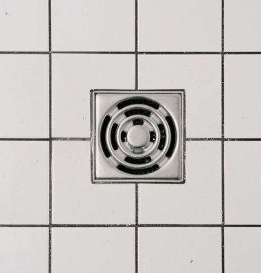 Square metal floor drain centered in white tiled floor