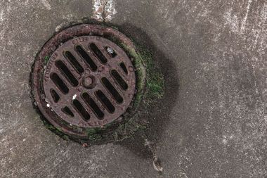 Round metal drain grate set in a weathered concrete surface with moss around the edge