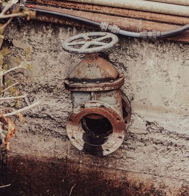 Rusty metal valve on a weathered wall with pipes above it