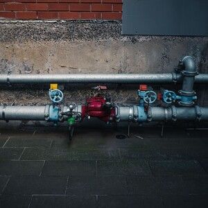 Industrial pipes and valves with a red pump against a concrete wall outdoors