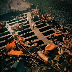 Rusty metal grate covered with dried leaves and debris in a dark, gritty setting