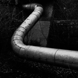 Curved metal pipe running through a dark, gritty concrete wall opening