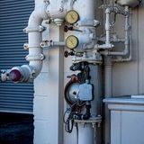 Industrial pipes and pressure gauges mounted on a building exterior near a garage door