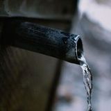 Water pouring from a black pipe into a blurred outdoor setting