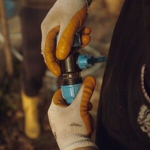 Gloved hands adjusting a blue water valve on a pipe outdoors